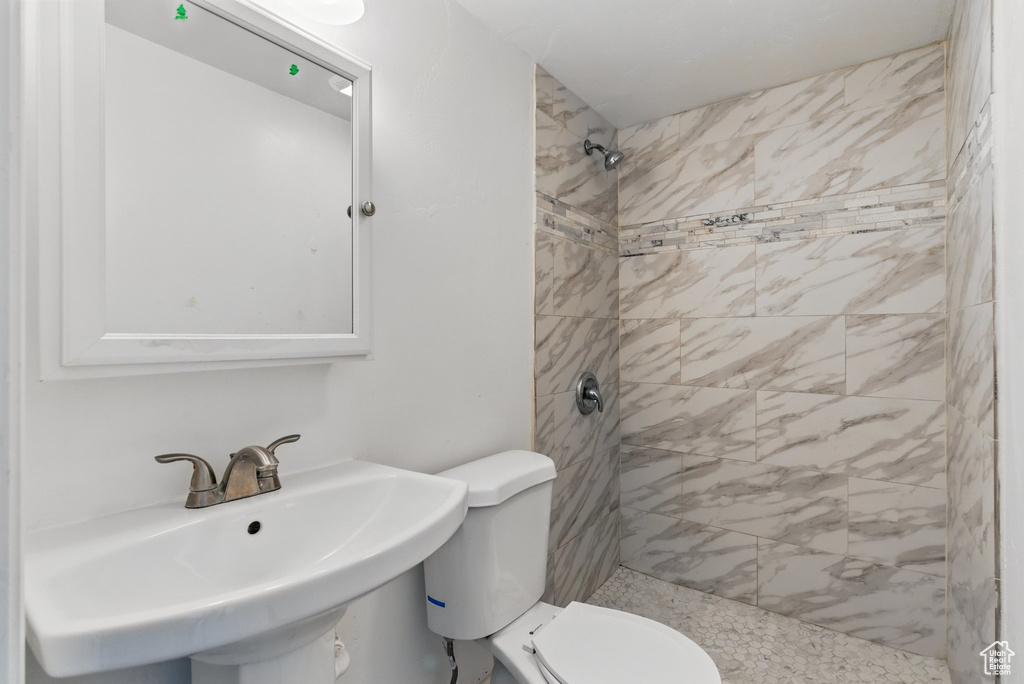 Full bath featuring tiled shower, a sink, and toilet