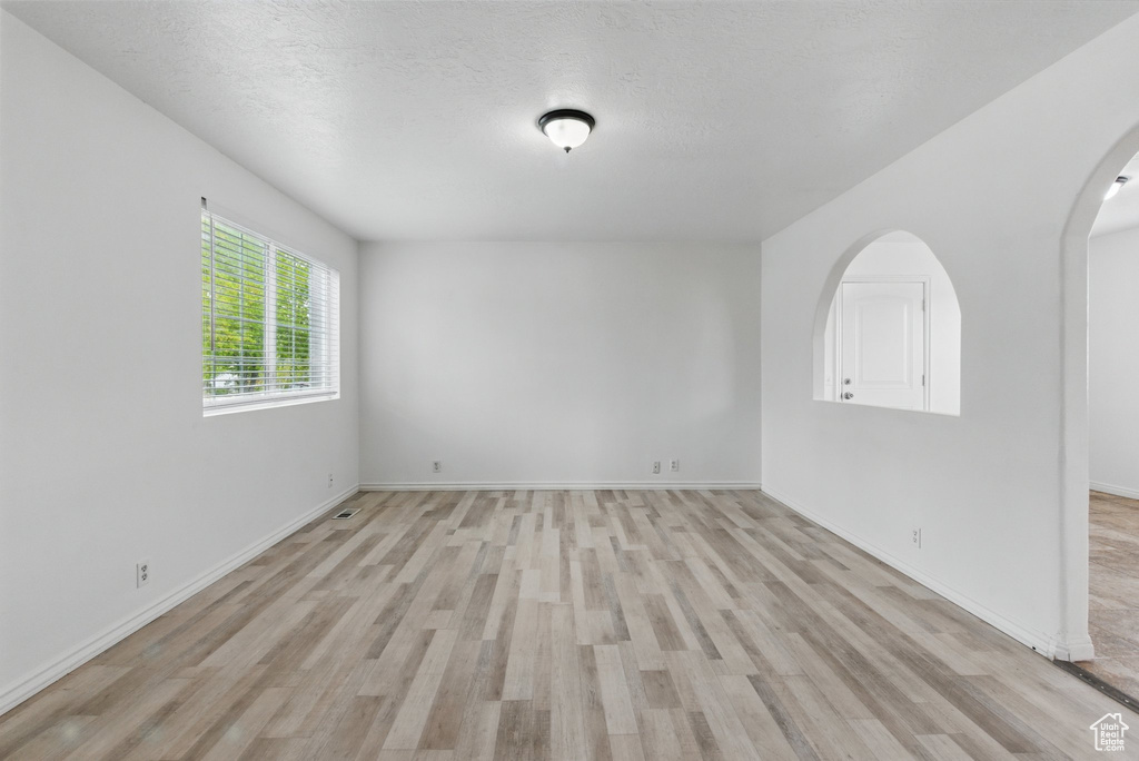 Spare room with arched walkways, light wood-style floors, and baseboards