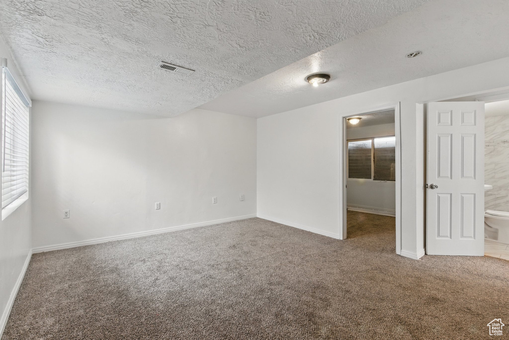 Empty room featuring carpet flooring, baseboards, and a textured ceiling