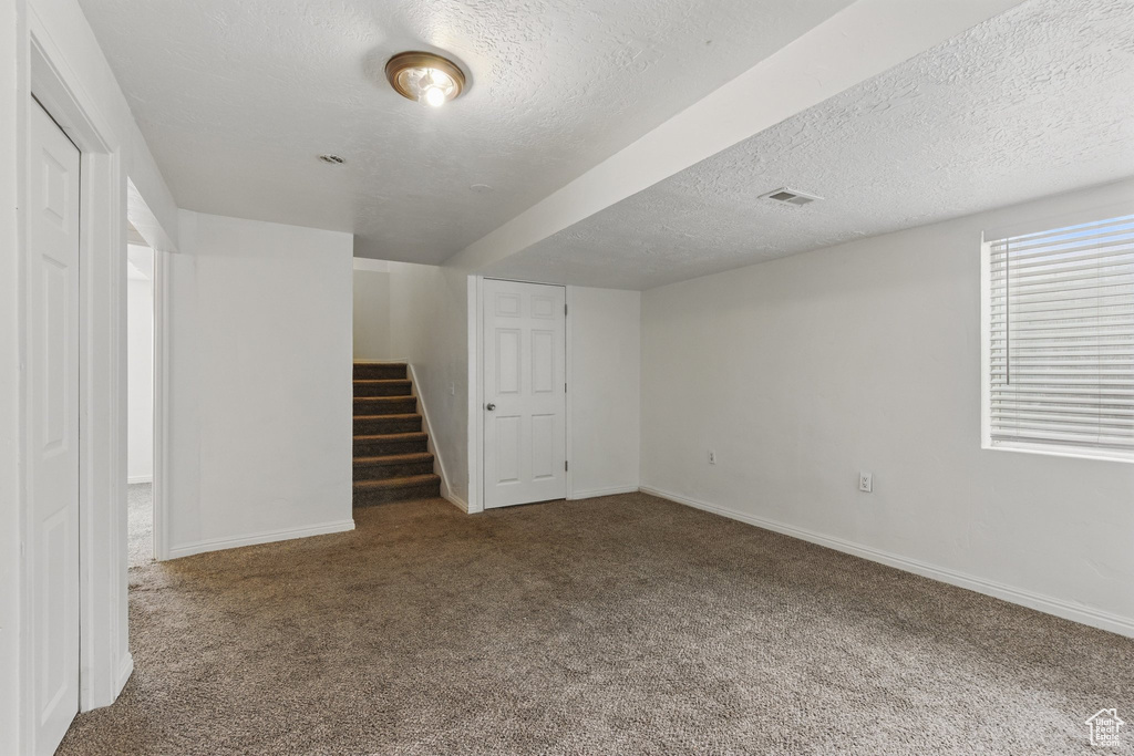 Below grade area featuring carpet floors, stairs, a textured ceiling, and baseboards