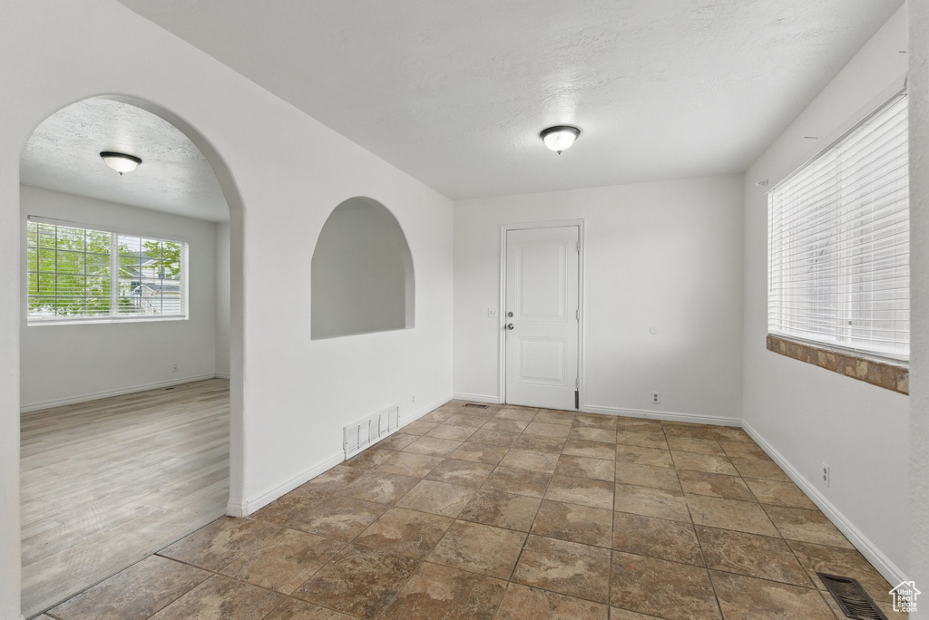 Unfurnished room with baseboards, a textured ceiling, arched walkways, and stone finish flooring