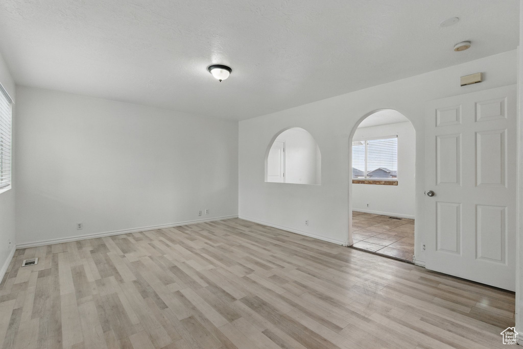 Unfurnished room featuring light wood-type flooring, baseboards, and arched walkways