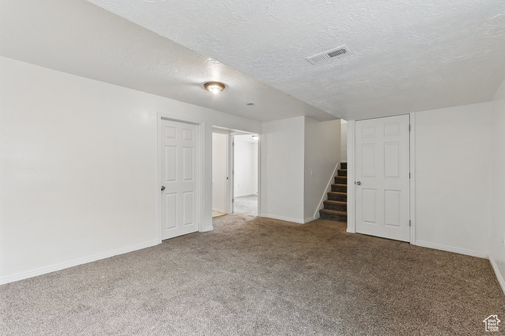 Finished basement with carpet, stairs, baseboards, and a textured ceiling