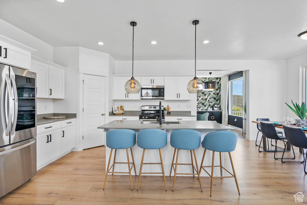 Kitchen featuring stainless steel appliances, recessed lighting, light wood-style floors, a kitchen breakfast bar, and white cabinetry