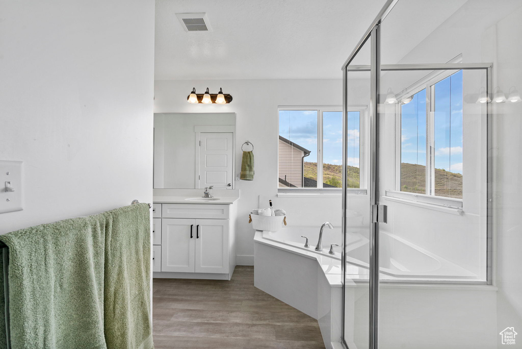 Full bathroom featuring vanity, wood finished floors, a garden tub, a shower stall, and baseboards