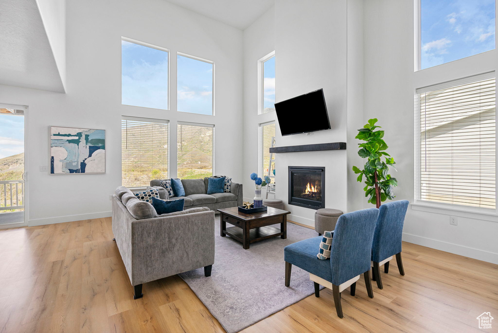 Living area featuring light wood-style floors, a high ceiling, a glass covered fireplace, and baseboards