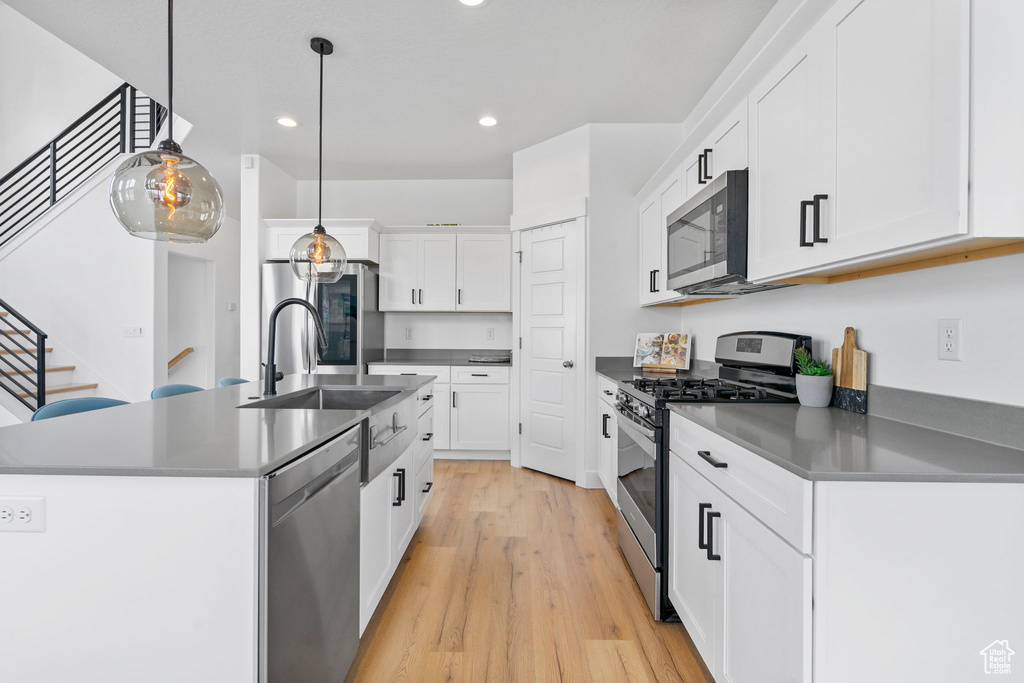 Kitchen featuring stainless steel appliances, dark countertops, light wood-style flooring, a sink, and recessed lighting