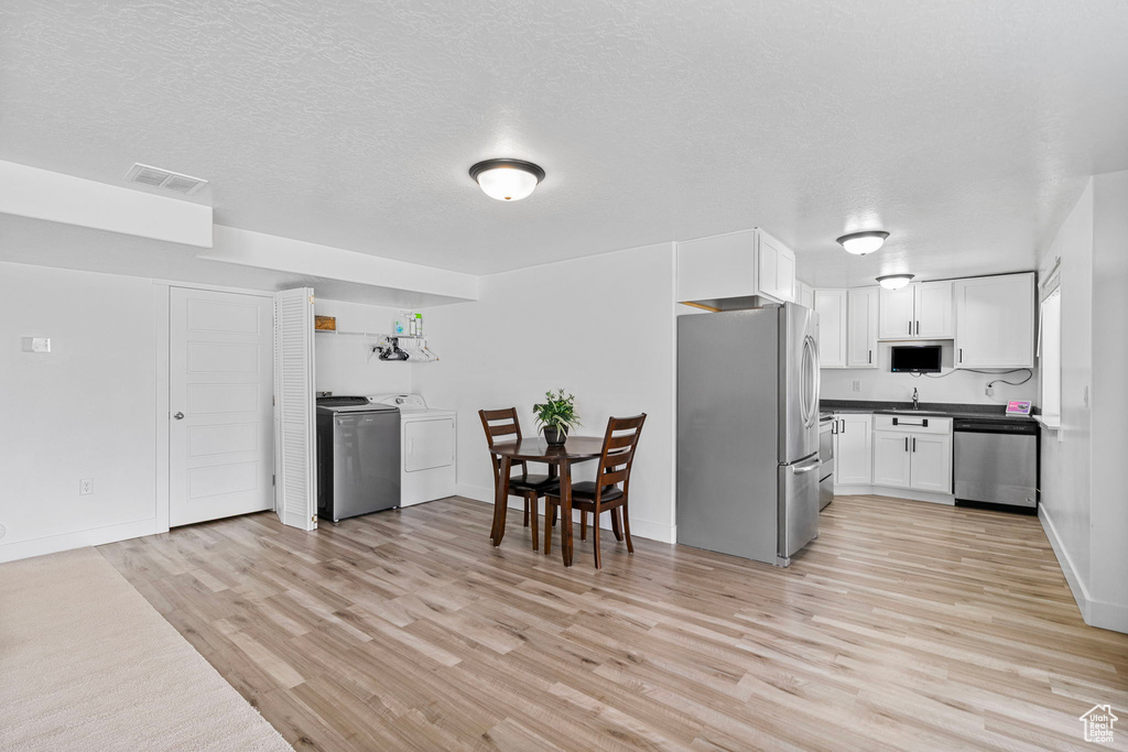 Kitchen featuring stainless steel appliances, washer / clothes dryer, light wood-style flooring, white cabinets, and a textured ceiling