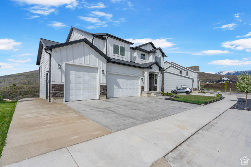 Modern farmhouse featuring board and batten siding, driveway, stone siding, a mountain view, and a garage