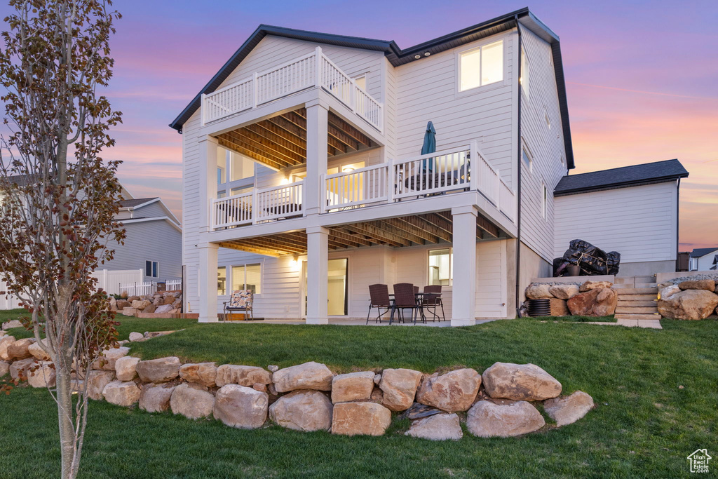Back of house at dusk featuring a balcony, a patio, and a yard