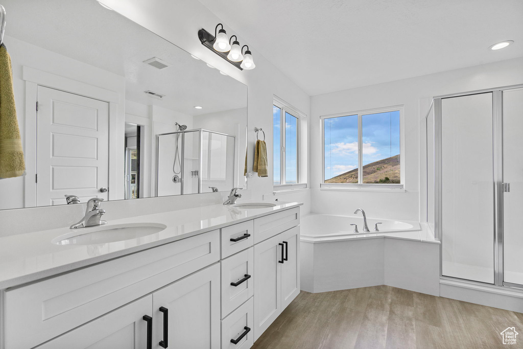 Bathroom with a stall shower, wood finished floors, double vanity, a garden tub, and recessed lighting