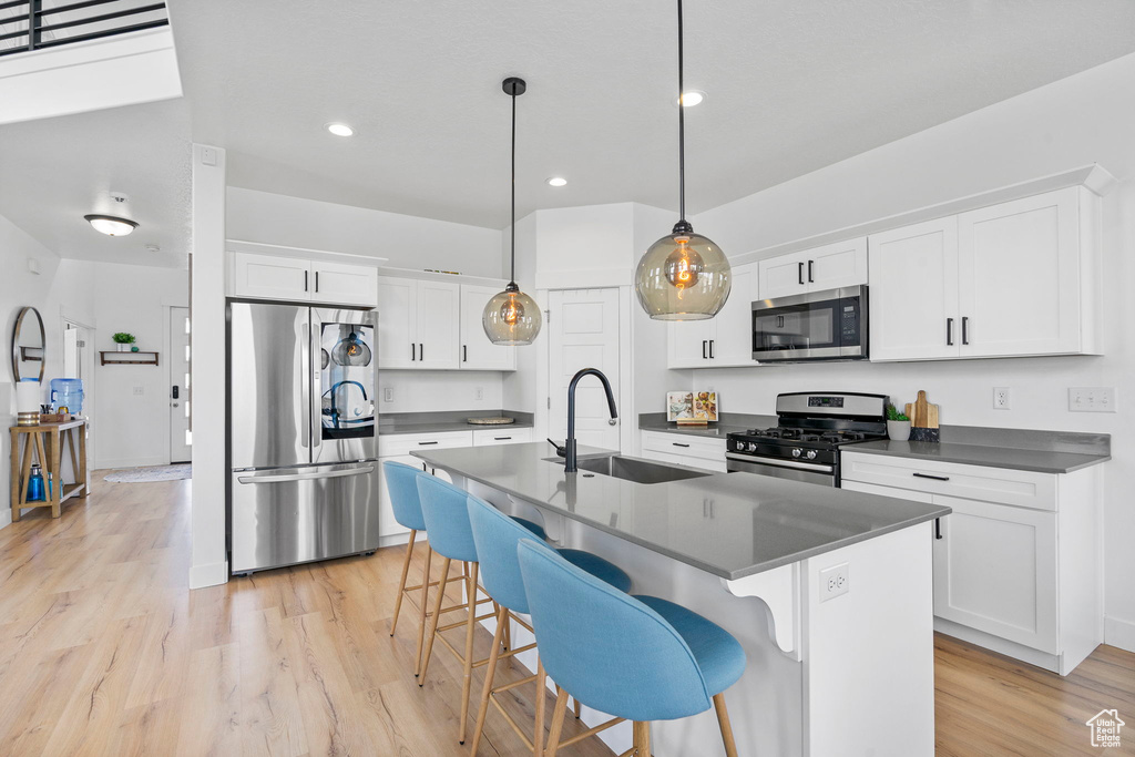 Kitchen featuring appliances with stainless steel finishes, a sink, dark countertops, light wood finished floors, and recessed lighting
