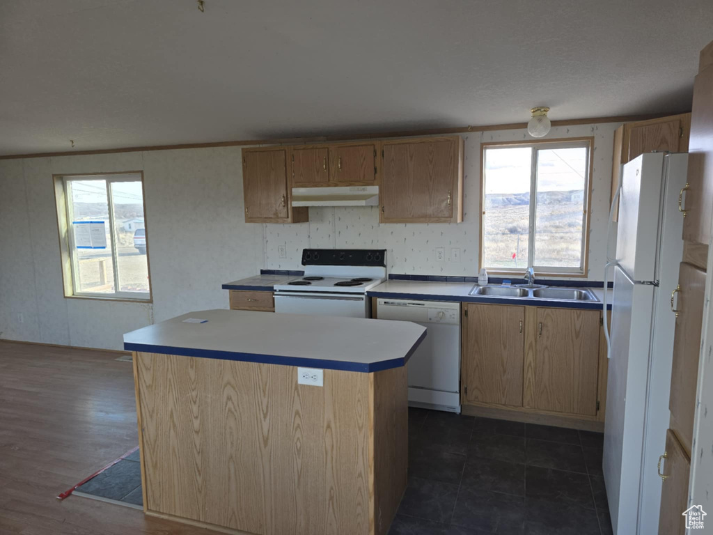 Kitchen featuring white appliances, a sink, under cabinet range hood, a center island, and plenty of natural light