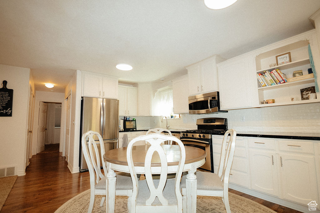 Kitchen featuring appliances with stainless steel finishes, tasteful backsplash, white cabinets, wood finished floors, and open shelves
