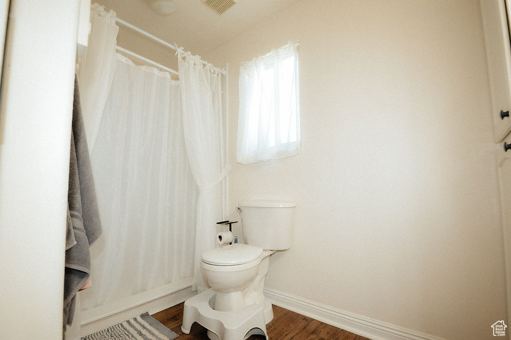 Bathroom with wood finished floors, baseboards, toilet, and a shower with curtain