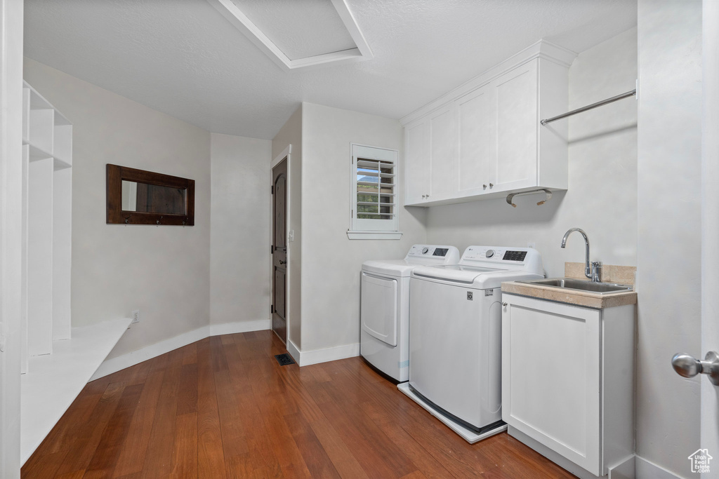 Clothes washing area featuring washing machine and dryer, dark wood-type flooring, cabinet space, attic access, and baseboards
