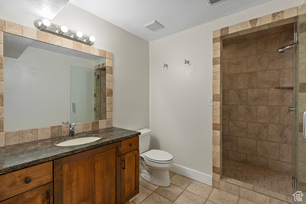Full bathroom featuring a stall shower, toilet, tile patterned floors, vanity, and a textured ceiling