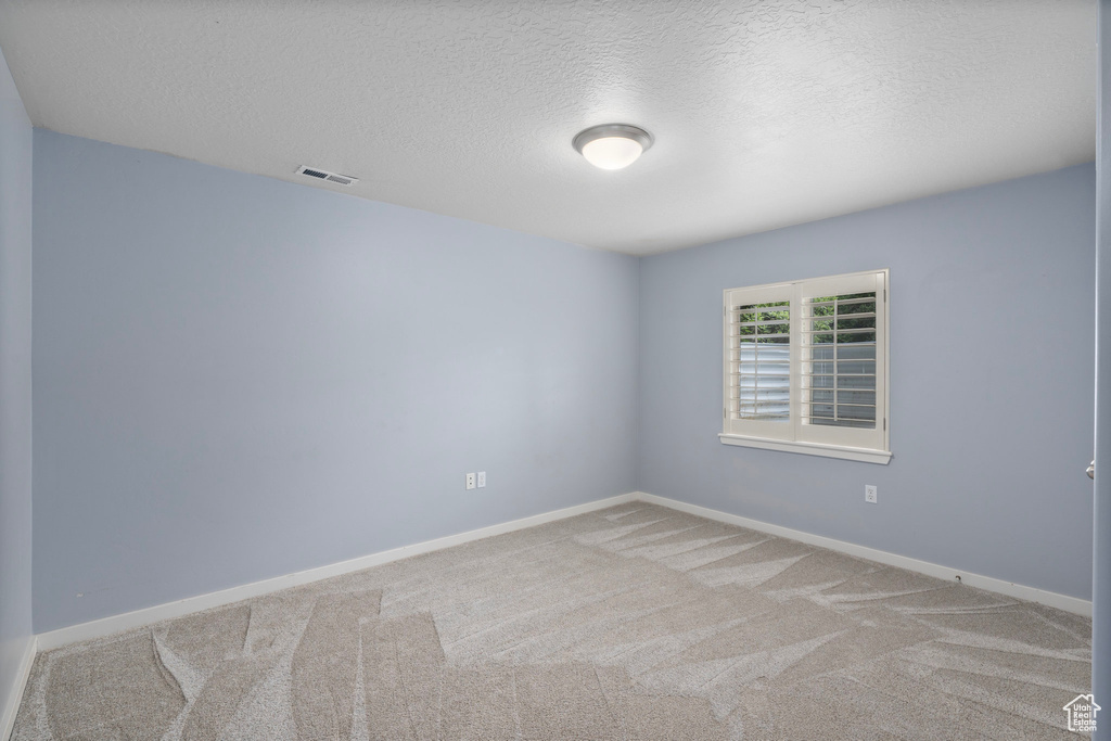 Carpeted spare room with a textured ceiling and baseboards