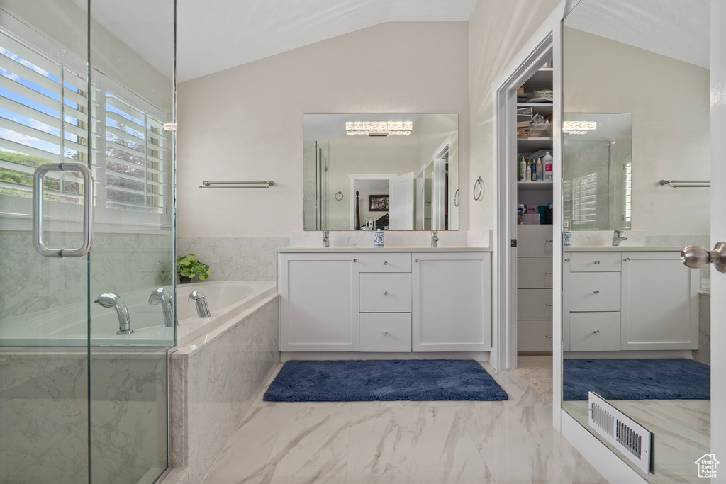 Full bathroom featuring lofted ceiling, marble look tiles, a bath, two vanities, and an enclosed shower