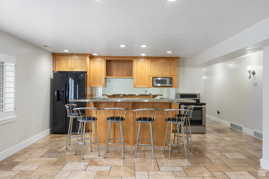 Kitchen featuring stainless steel appliances, baseboards, stone tile flooring, recessed lighting, and a textured ceiling
