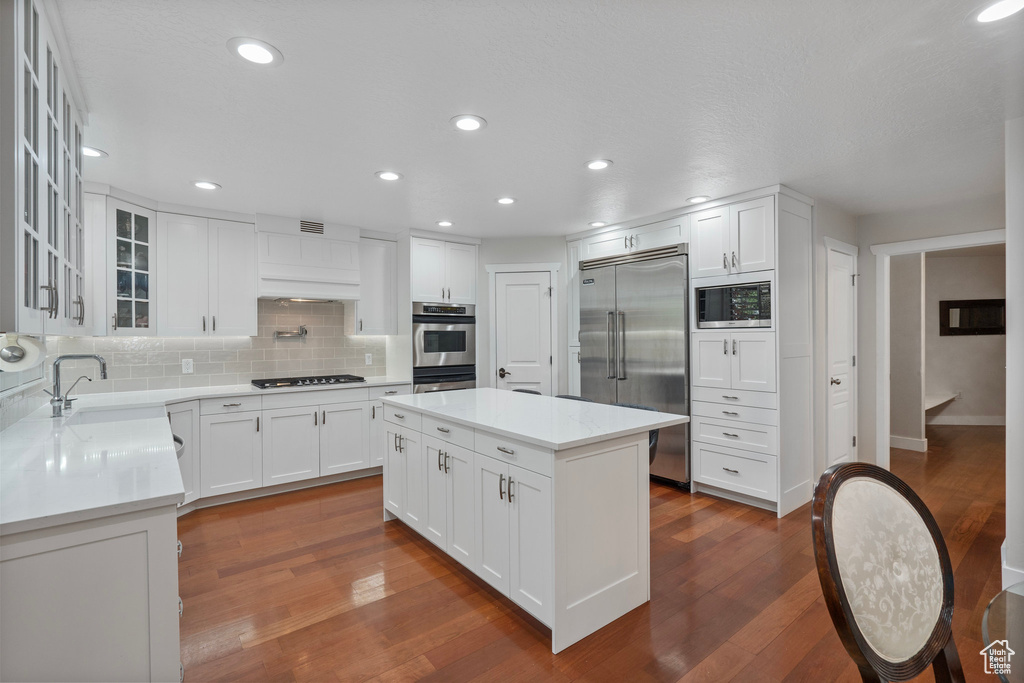 Kitchen featuring built in appliances, decorative backsplash, dark wood finished floors, light countertops, and a center island