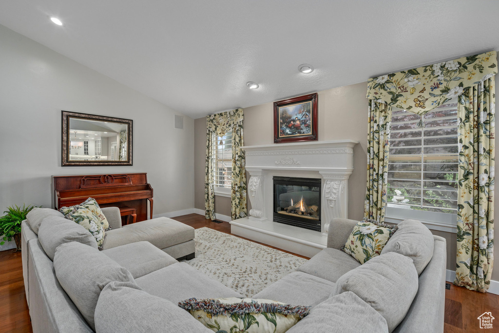 Living room featuring vaulted ceiling, a glass covered fireplace, wood finished floors, baseboards, and recessed lighting