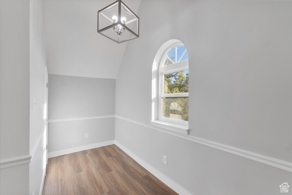 Interior space featuring baseboards, vaulted ceiling, a notable chandelier, and wood finished floors