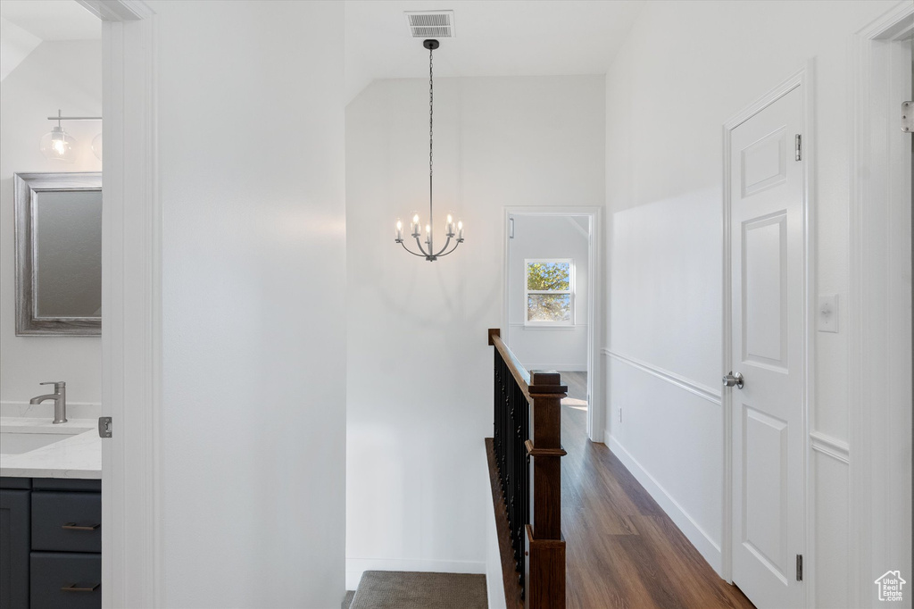 Staircase with an inviting chandelier, wood finished floors, high vaulted ceiling, visible vents, and baseboards