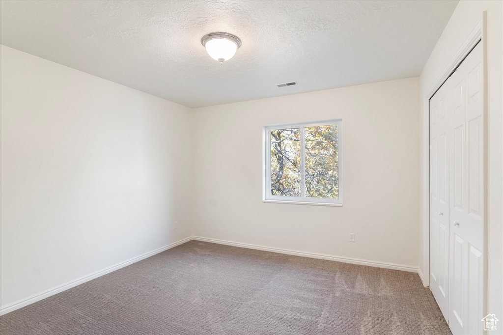 Unfurnished bedroom with carpet flooring, a closet, visible vents, and a textured ceiling