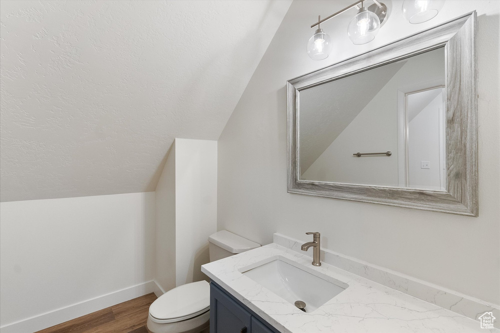 Bathroom with lofted ceiling, toilet, wood finished floors, vanity, and baseboards