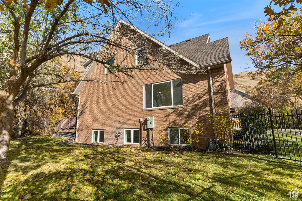 Rear view of house featuring a shingled roof, brick siding, fence, and a lawn