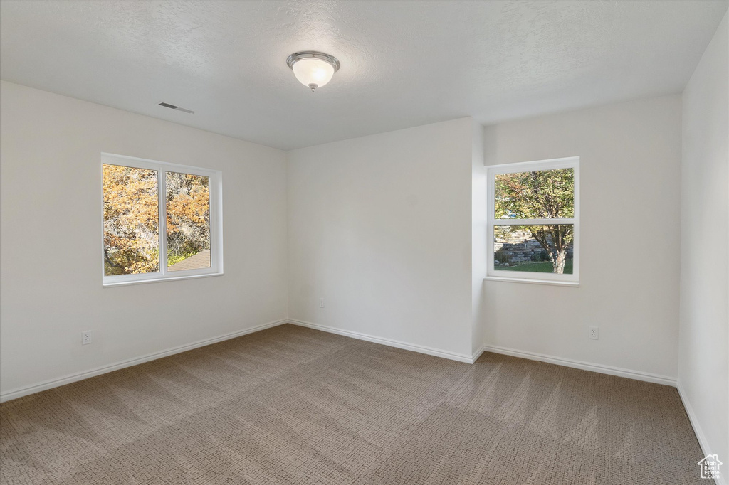 Unfurnished room with a textured ceiling, visible vents, baseboards, and carpet floors