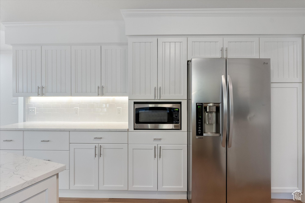 Kitchen with tasteful backsplash, ornamental molding, light stone counters, white cabinets, and appliances with stainless steel finishes
