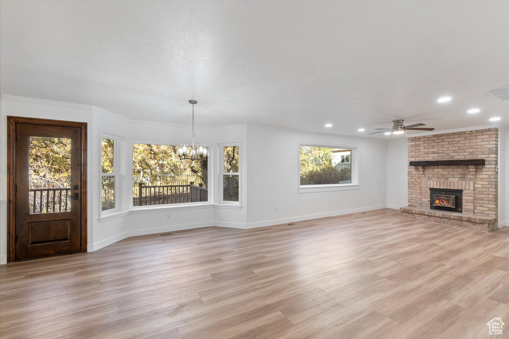 Unfurnished living room featuring light wood-style flooring, recessed lighting, baseboards, ceiling fan with notable chandelier, and a fireplace