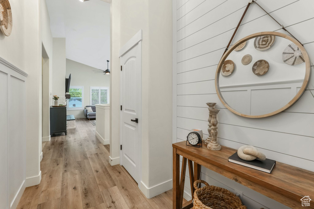 Hallway featuring light wood finished floors, baseboards, and vaulted ceiling