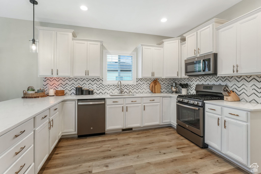 Kitchen with appliances with stainless steel finishes, a sink, white cabinets, light countertops, and backsplash