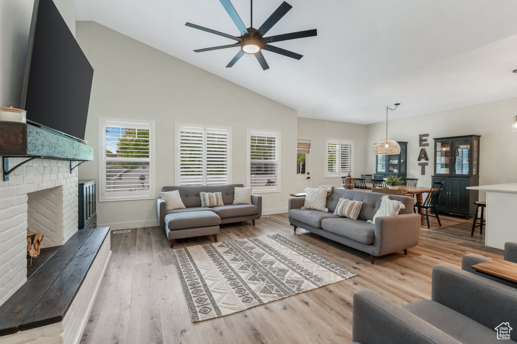 Living area featuring a ceiling fan, a brick fireplace, light wood-style flooring, high vaulted ceiling, and baseboards