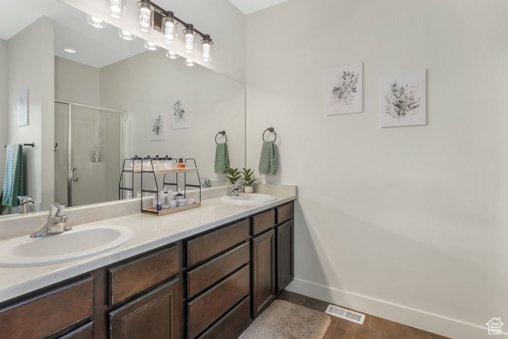 Bathroom featuring a shower stall, double vanity, tile patterned flooring, and baseboards