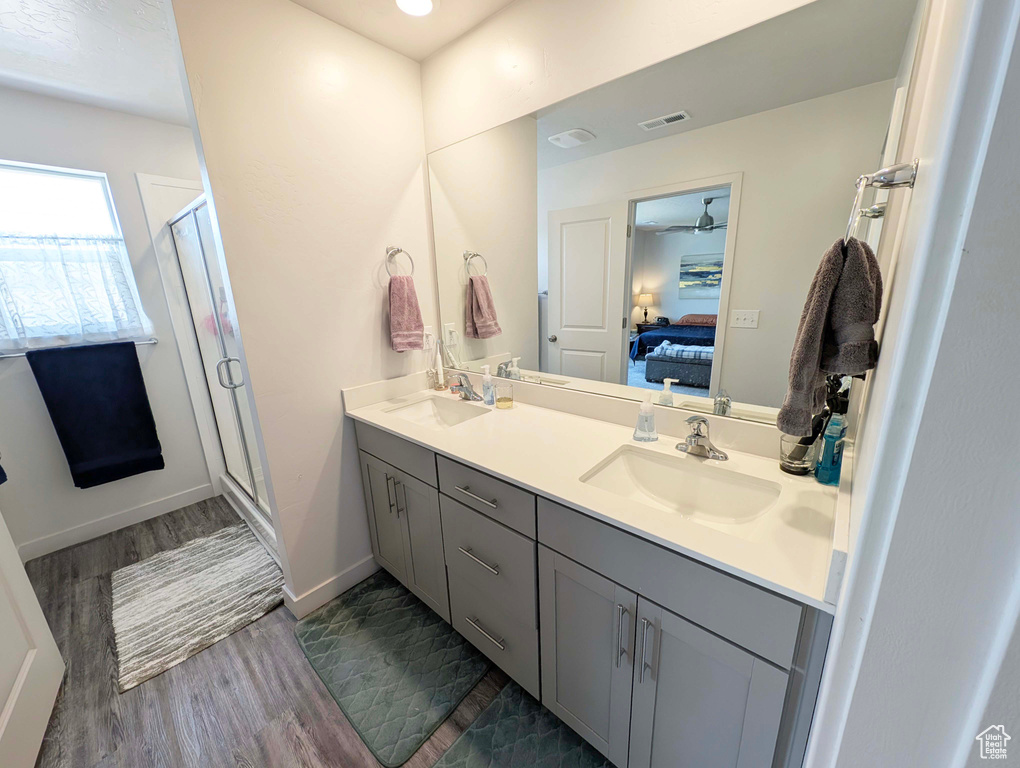Full bath with ensuite bathroom, double vanity, a stall shower, wood finished floors, and a ceiling fan