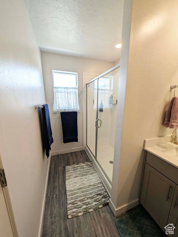 Bathroom featuring wood finished floors, a shower stall, baseboards, vanity, and a textured ceiling