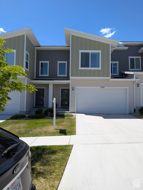 View of property with board and batten siding, an attached garage, driveway, and a front lawn