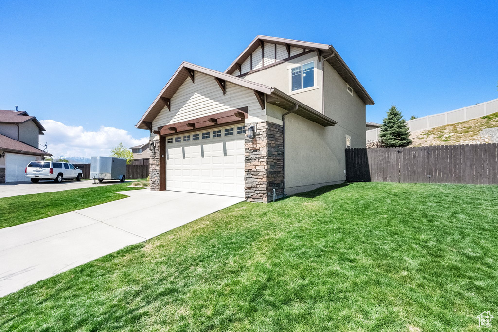 View of property exterior with stone siding, driveway, fence, and a yard