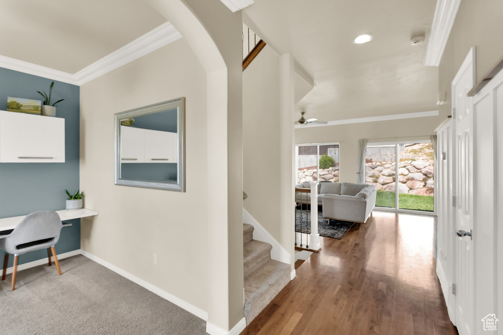 Hall with arched walkways, baseboards, wood finished floors, stairs, and ornamental molding