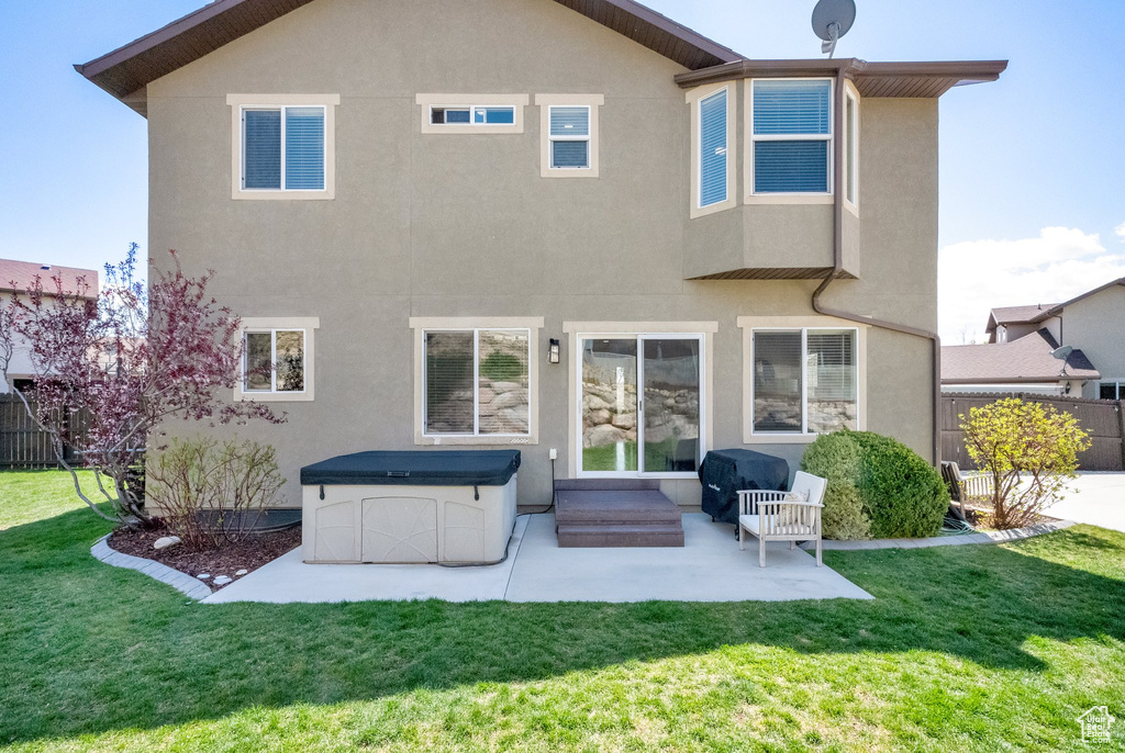 Rear view of property featuring stucco siding, fence, a patio area, and a lawn