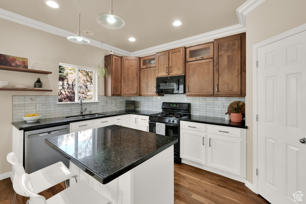 Kitchen with a sink, glass insert cabinets, crown molding, decorative light fixtures, and black appliances