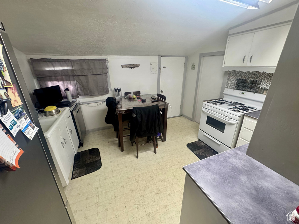 Kitchen with light floors, white gas range, backsplash, white cabinets, and baseboards