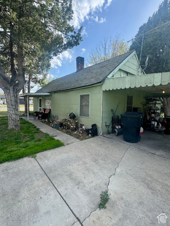View of property exterior with a shingled roof, driveway, a chimney, and a carport