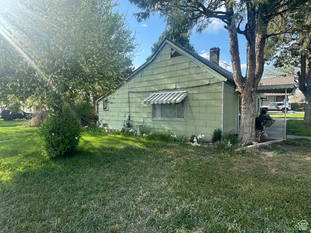 View of property exterior featuring a chimney and a lawn