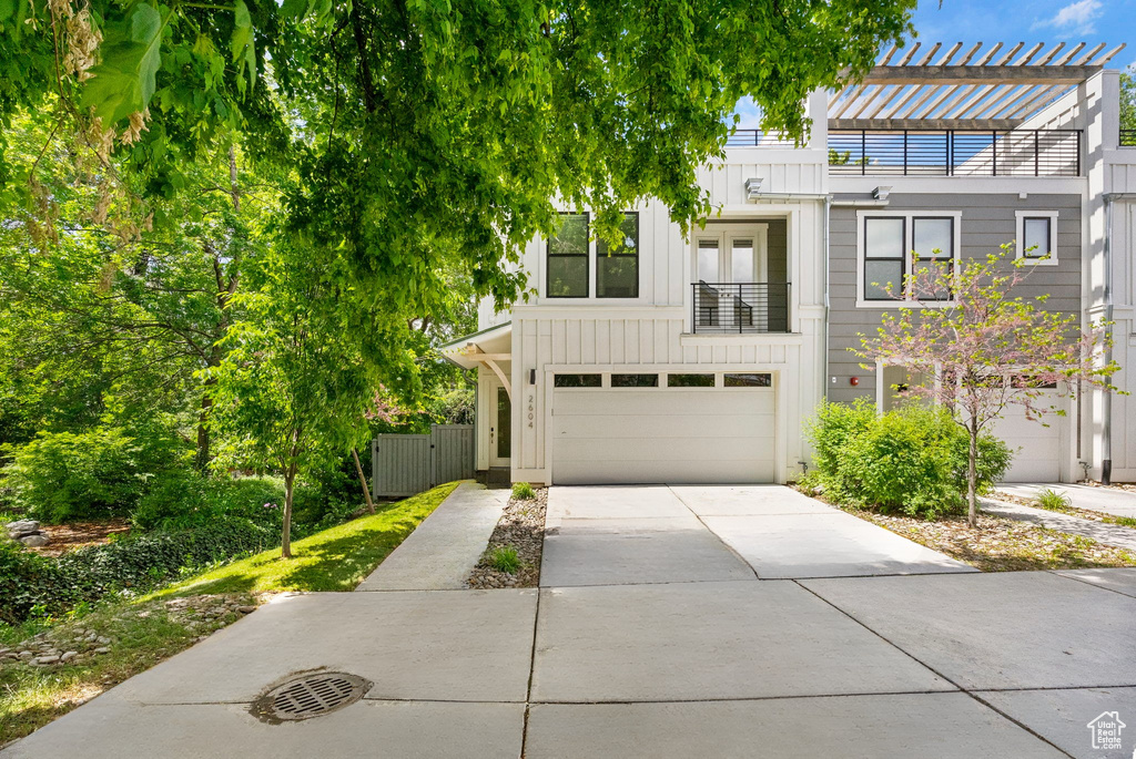 View of property featuring board and batten siding, an attached garage, driveway, and a balcony