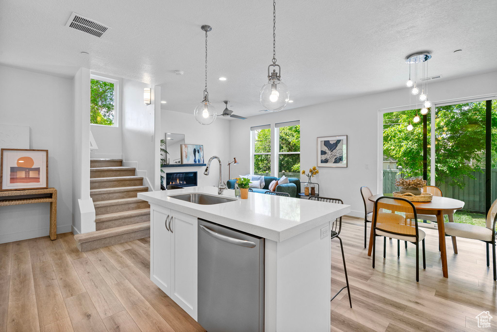 Kitchen with a sink, dishwasher, a glass covered fireplace, an island with sink, and light countertops